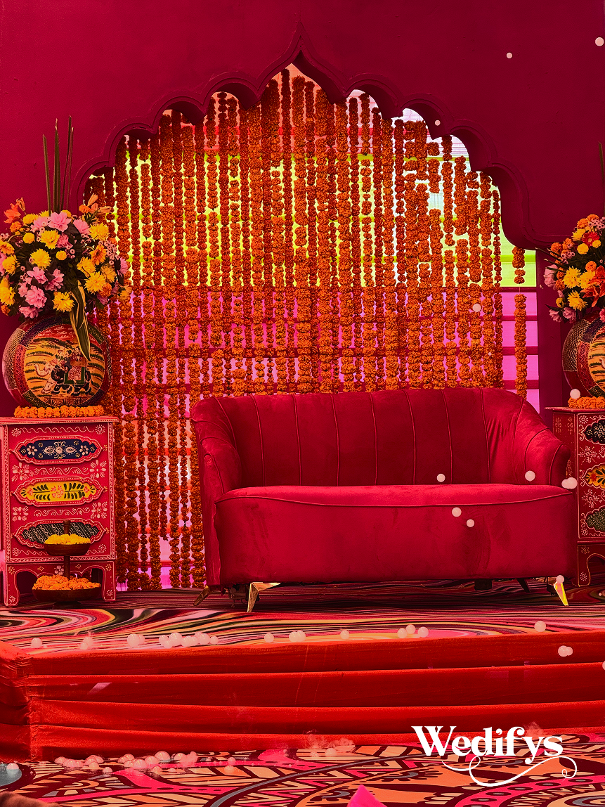 Haldi-Couple-Stage-with-Marigold-Backdrop-and-Velvet-Red-Sofa-04242026